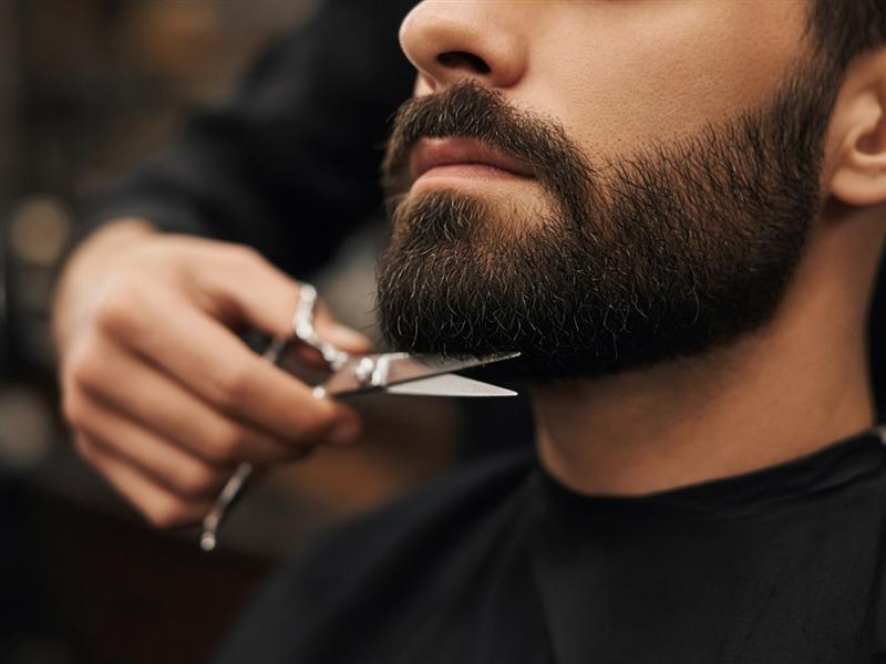 Barbeiro aparando a barba de um cliente com tesoura